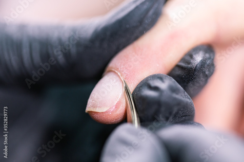 Close-up professional beautician hands working with electric drill on client fingernails. Procedure applying artificial fingernails. Hands of manicurist with tool. Manicurist in gloves removes cuticle