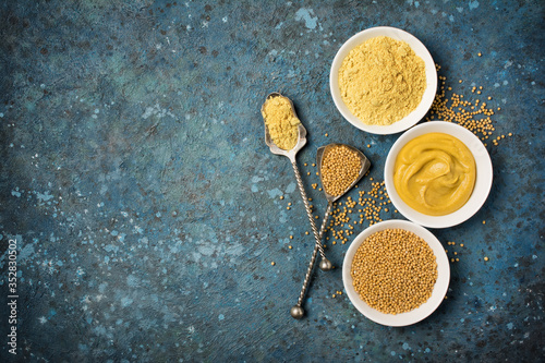 Set of yellow mustard sauce, powder and seeds in small bowls with silver spoons