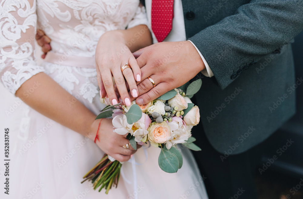 Hands of the newlyweds with wedding gold rings on their fingers and a bouquet of fresh flowers. Wedding close-up portrait. Photography, concept. Hands of the newlyweds with wedding gold rings on their fingers and a bouquet of fresh flowers. Wedding close-up portrait. Photography, concept.