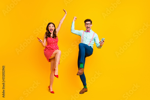 Full length photo attractive lady handsome guy couple hold telephones win lottery online scream achievement wear red dotted dress shirt bowtie retro clothes isolated yellow color background