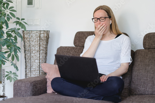 frau arbeitet zu hause auf der Couch am laptop, ist müde und gähnt