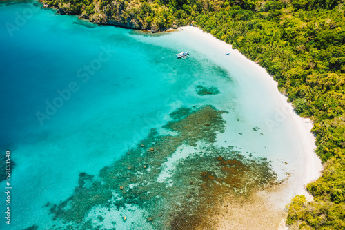Aerial drone view of lonely boat at beautiful deserted tropical beach and blue lagoon surrounded by lush green jungle. Cadlao Island, El Nido, Palawan, Philippines © Igor Tichonow