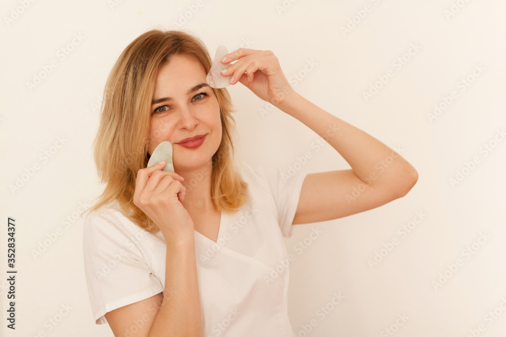 Beautiful young woman receiving Guasha face drainage massage with jade stone Beautiful young woman receiving Guasha face drainage massage with jade stone