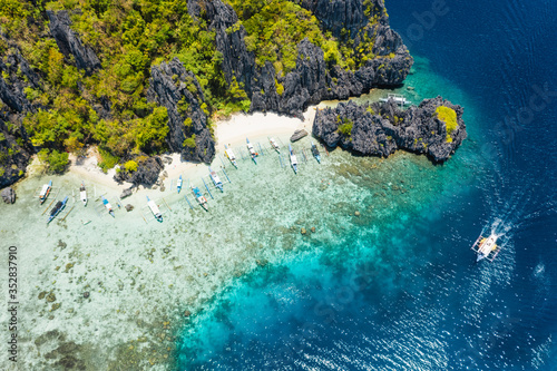 Fototapeta Naklejka Na Ścianę i Meble -  Aerial drone view tourism boats moored at tropical Shimizu Island. Limestone coastal rocks, white sand beach in blue water. El Nido, Palawan, Philippines