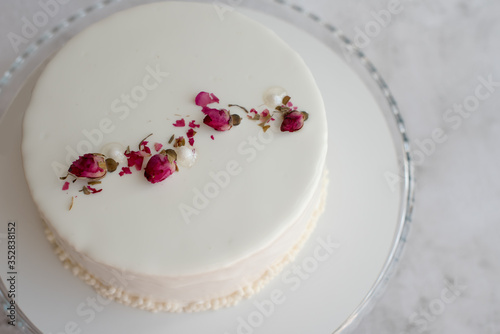 White mousse cake decorated with dried rose buds with milk and berry filling, close up. Copy space, place for text