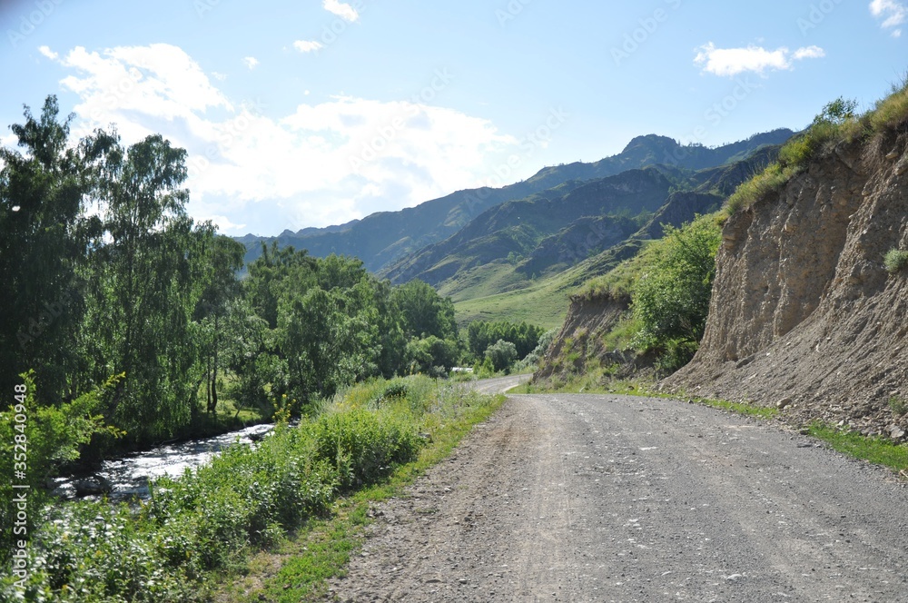 Dirt road near the river, trees and mountains