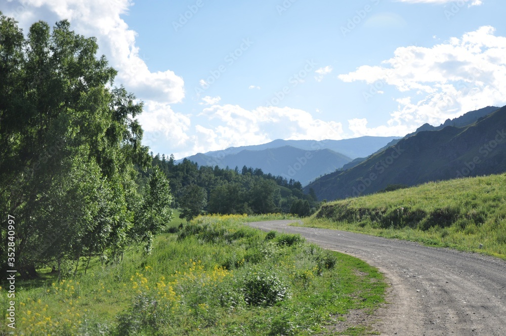 Turn of dirt road near trees, mountainside and clouds in the sky
