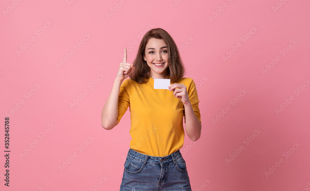 Young smiling beautiful woman in yellow shirt showing credit card in hand over pink background. Young smiling beautiful woman in yellow shirt showing credit card in hand over pink background.