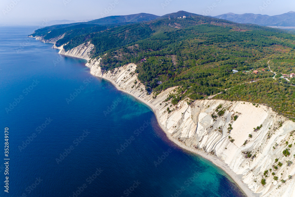The coast of the Black sea near Gelendzhik. High layered rocks covered with pine trees. Gorges form a descent to the sea. A small pebble beach at the foot of the cliffs