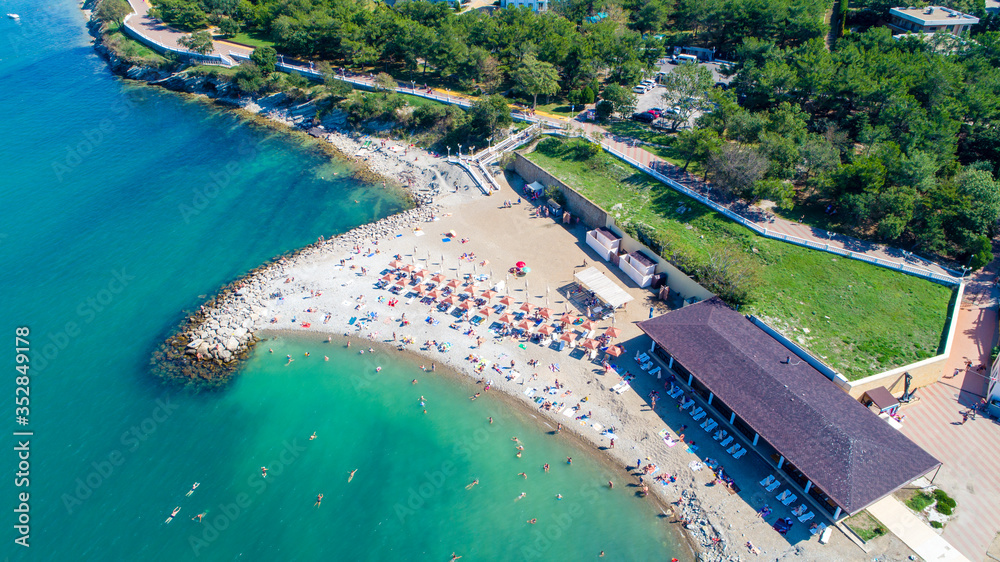 Beach of Gelendzhik resort. Numerous sun umbrellas and sun loungers. Embankment with balustrade. Houses and trees behind the embankment