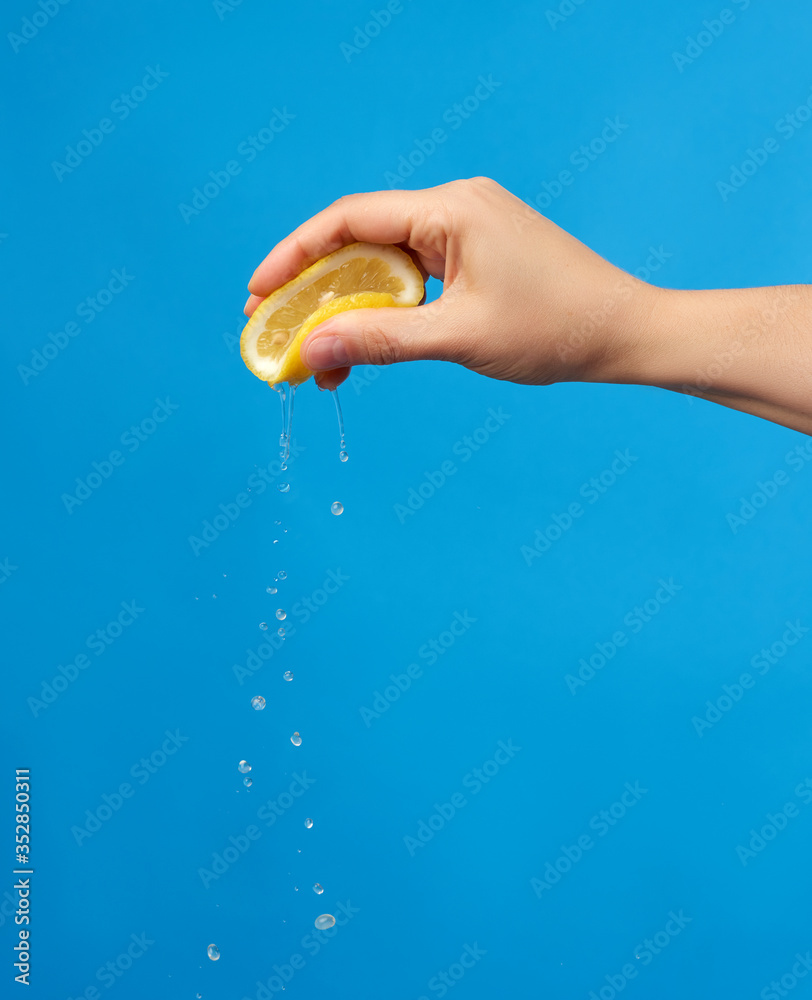 female hand holds half a yellow lemon and squeezes it on a blue background