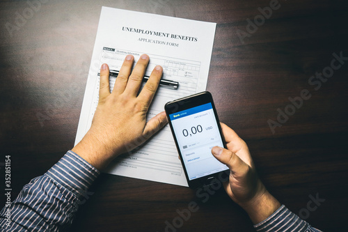 A man checks her account balance on phone. Lack of money, filling out unemployment benefits form.  All screen graphics are made up. Concept of coronavirus and stay at home order impact on economy photo