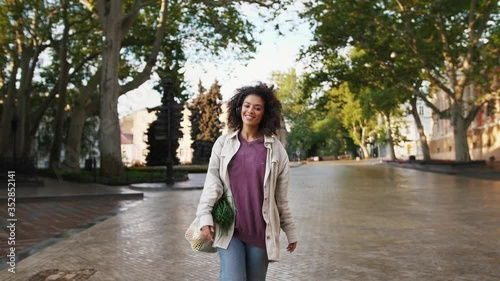 African american girl with afro hairstyle, in headphones and casual clothes. She smiling, dancing, listening to the music while walking in a city photo
