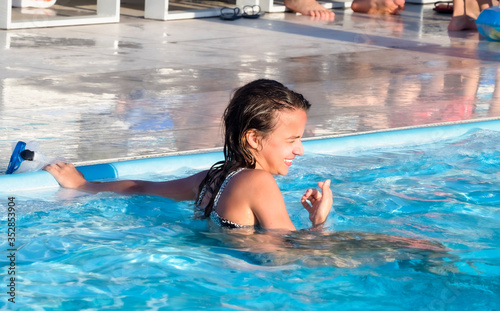 Happy smiling girl having fun and playing in the swimming pool at the summer day time, summertime outdoor