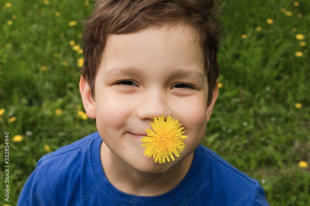 A portrait of happy boy with a yellow dandelion in his mouth on a background of green grass. The concept of children's day. A portrait of happy boy with a yellow dandelion in his mouth on a background of green grass. The concept of children's day.