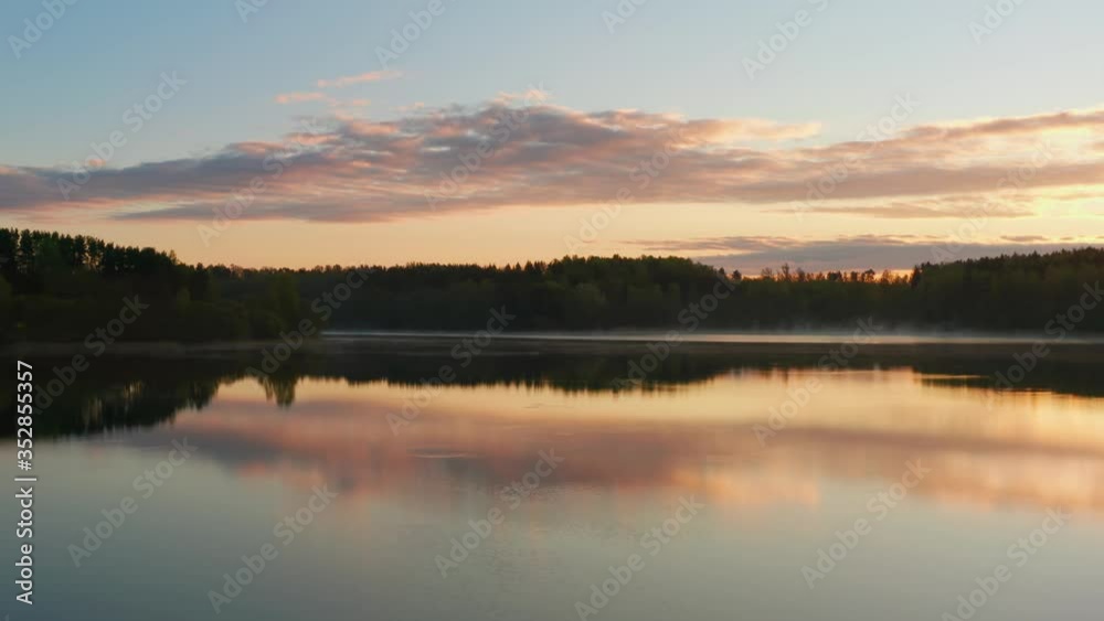 Flying over lake at sunrise. Clouds of fog above water surface. Early morning mist haze. Haze over river countryside. Pine trees on horizon reflected in water as in mirror. Beautiful dawn landscape Flying over lake at sunrise. Clouds of fog above water surface. Early morning mist haze. Haze over river countryside. Pine trees on horizon reflected in water as in mirror. Beautiful dawn landscape