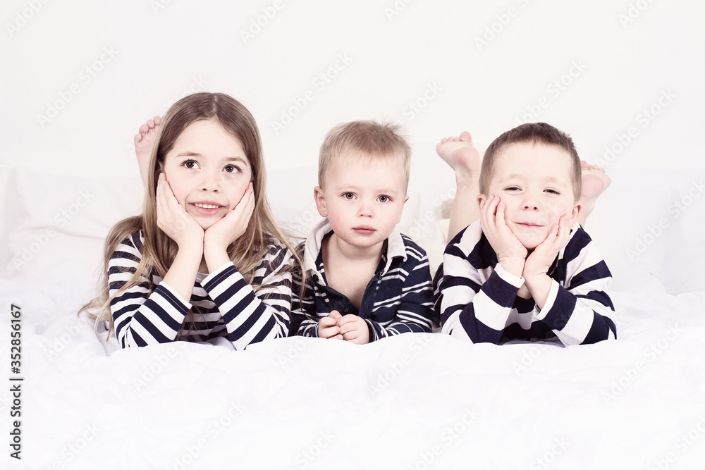 Three siblings lying on white bed in striped pyjamas Three siblings lying on white bed in striped pyjamas