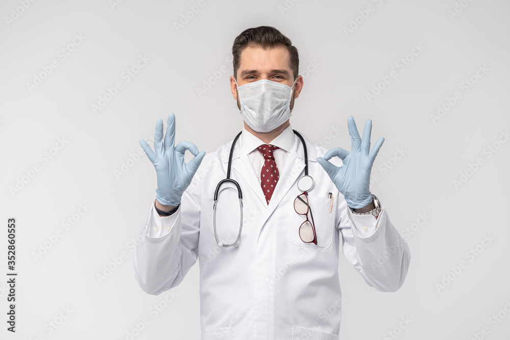 Coronavirus. COVID-19 pandemic. Attractive handsome doctor in protective face mask, white lab coat isolated on white