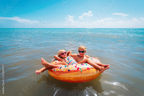 Photography happy kids, boy and girl, swim on floatie at beach