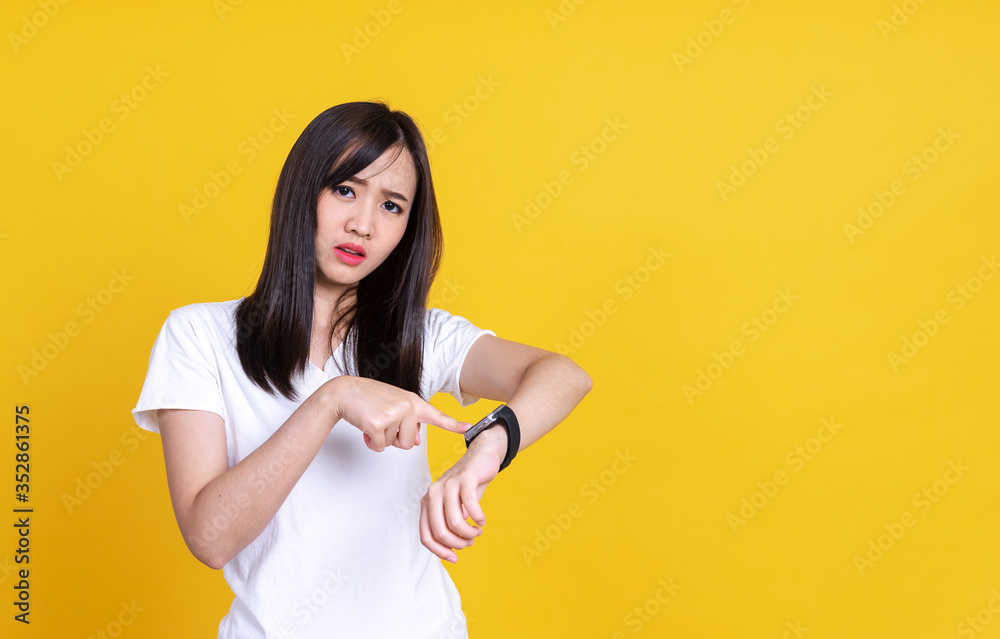 Portrait of young Asian woman holding hand with wrist watch and looking or pointing to watch isolated on yellow background Portrait of young Asian woman holding hand with wrist watch and looking or pointing to watch isolated on yellow background