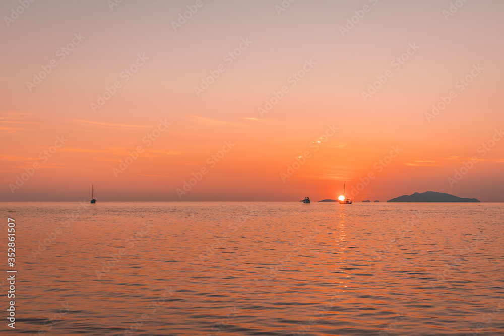 Romantic sunset at sea with sailboat sailing along its journey against orange and yellow color filled sky