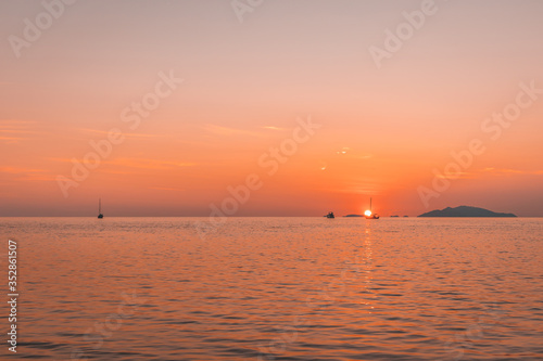 Romantic sunset at sea with sailboat sailing along its journey against orange and yellow color filled sky