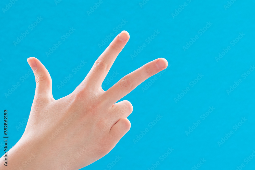 Close-up female hand showing and pointing up with number three fingers on blue background, copy space