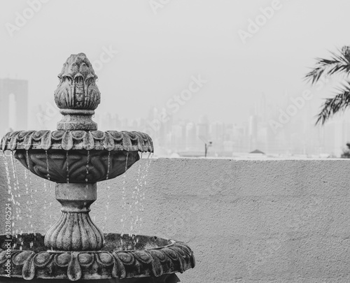 BLK&WHT photo of the small two-level fountain with a water jets falling down . City view at the backgroun photo