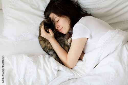 pets, morning, comfort, rest and people concept - happy young woman with cat in bed at home