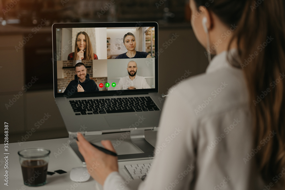 A Back view of a woman working remotely in a video conference with her colleagues during an online meeting. Partners in a video call. Multiethnic business team having a discussion in an online meeting
