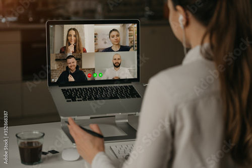 Obraz na płótnie A Back view of a woman working remotely in a video conference with her colleagues during an online meeting. Partners in a video call. Multiethnic business team having a discussion in an online meeting w salonie