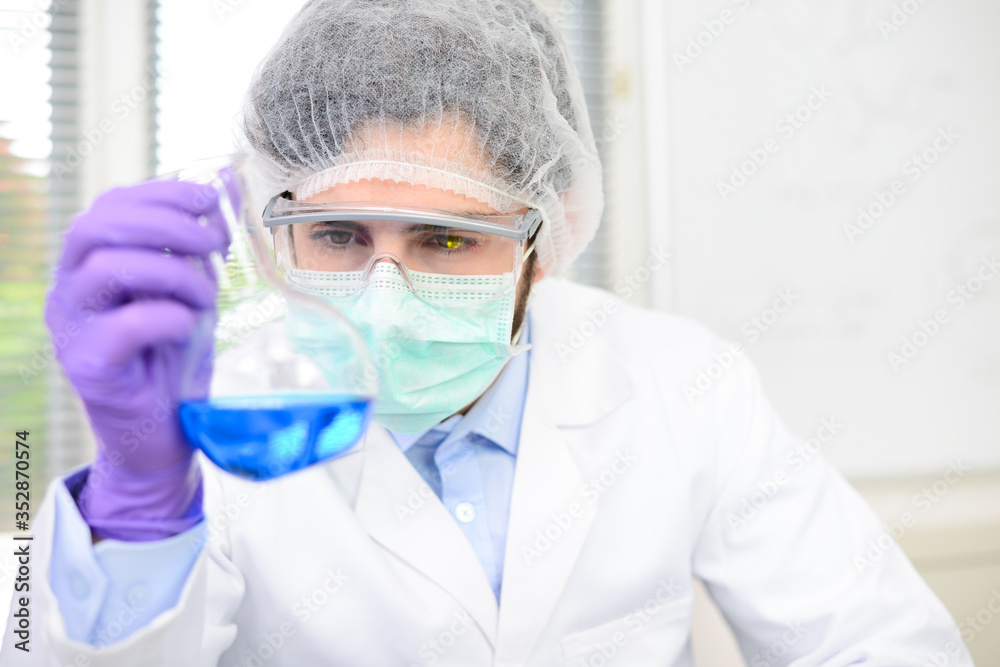 Young doctor scientist in the laboratory making experience research about covid19 coronavirus vaccine wearing white lab coat a mobcap and surgical mask