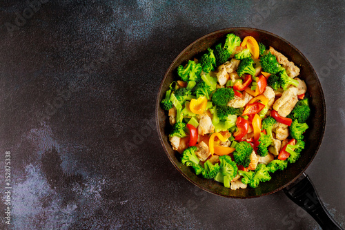 Colorful and healthy stir fry vegetables with chicken on dark surface.