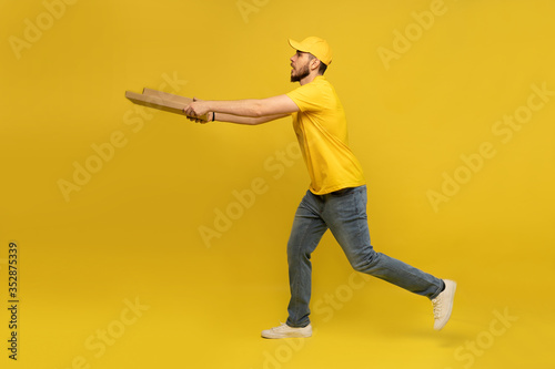 Portrait of young delivery man in yellow uniform with pizza boxes isolated over yellow background.