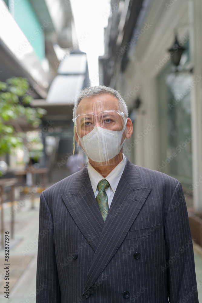Mature Japanese businessman with mask and face shield in the city