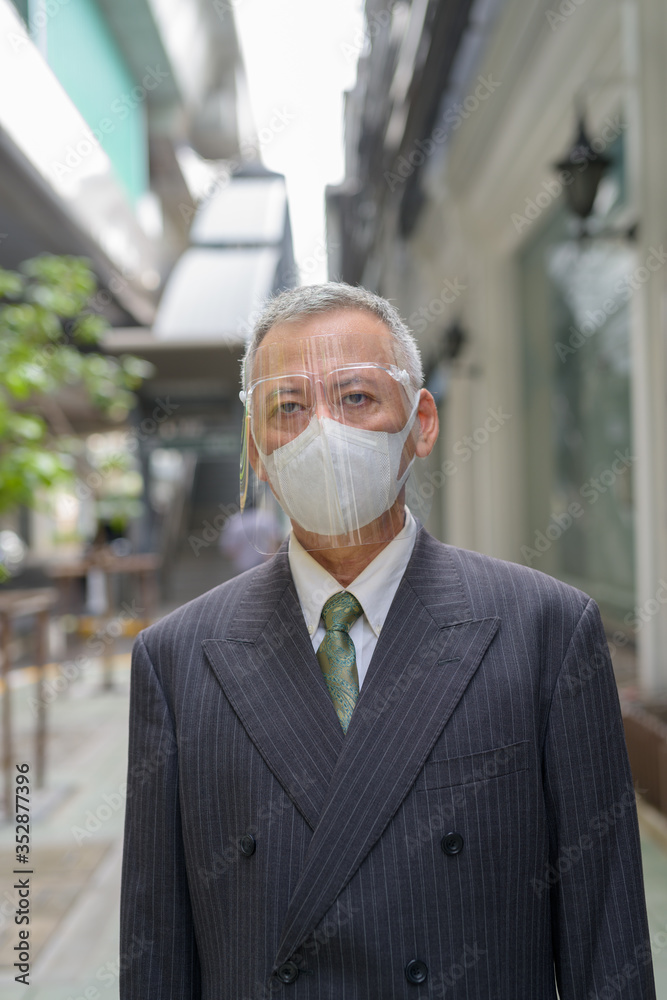 Mature Japanese businessman with mask and face shield in the city Mature Japanese businessman with mask and face shield in the city