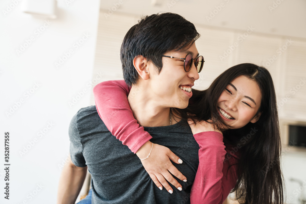 Photo of joyful asian man piggybacking nice woman and laughing Photo of joyful asian man piggybacking nice woman and laughing