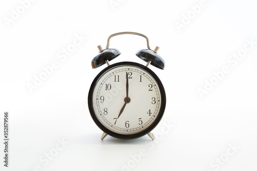 Black retro alarm clock isolated on white background. Copy space. Blank template backdrop. Early morning seven o'clock. Time to wake up. Selective focus