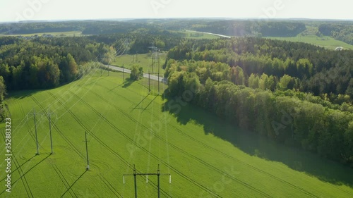Aerial high voltage steel power pylons in green field countryside. Flight over power transmission lines. Electric tower line, daylight, summer day