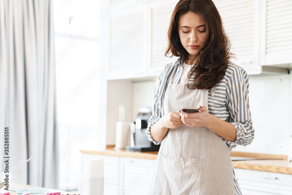 Image of focused brunette woman using cellphone while cooking pie Image of focused brunette woman using cellphone while cooking pie
