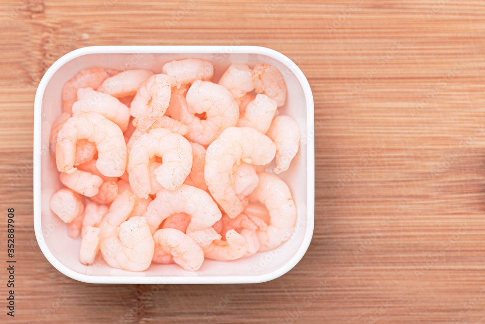 Boiled shrimps in white bowl on wooden kitchen board, top view