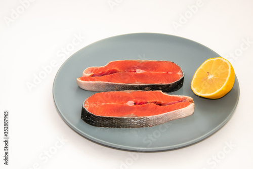 Close up fresh raw red fish steak with lemon slice on a plate, isolated on white background