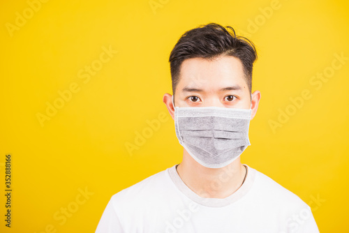 Closeup Asian young man wearing face mask protective germ virus or air dust, studio shot isolated on yellow background and copy space, medical outbreak coronavirus COVID-19 concept © sorapop