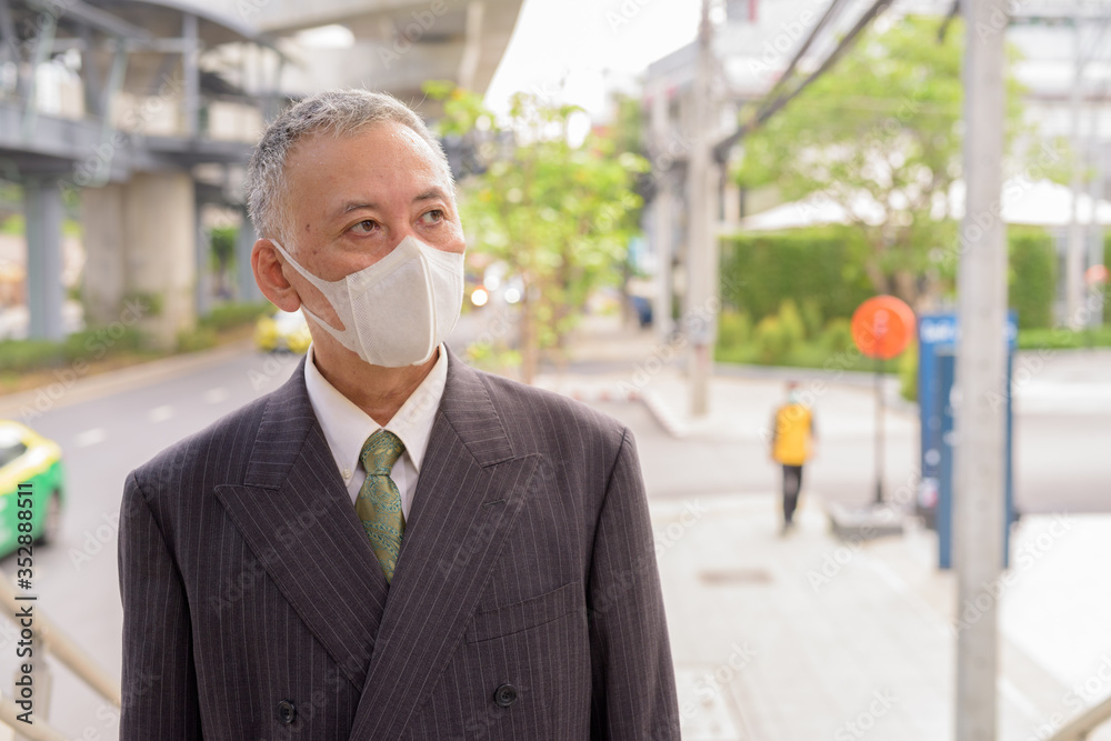 Mature Japanese businessman with mask thinking in the city Mature Japanese businessman with mask thinking in the city