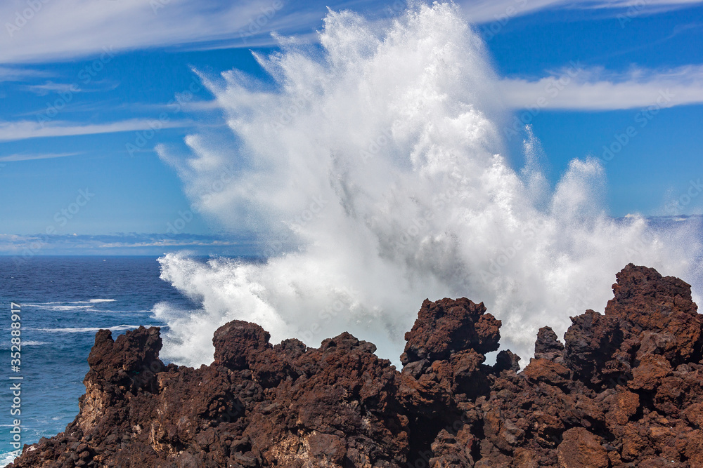 A big wave is crashing over a black rocks of volcanic coastline of Atlantic ocean on Tenerife island, Canary Islands, Spain