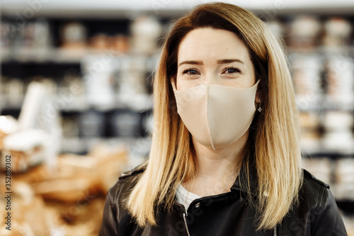 Portrait of a young pretty woman in a protective medical mask who is shopping at the supermarket during a pandemic. The buyer makes purchases at the grocery store.