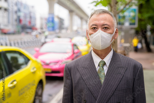 Mature Japanese businessman with mask waiting at the taxi station