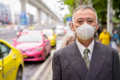 Mature Japanese businessman wearing mask at the taxi station