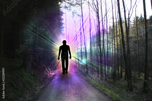black silhouette of a man with luminous rays of energy in a dark forest on the road among the trees, the concept of aura, living energy, death and the transition to another world