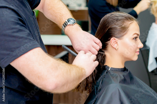 Women's haircut. Hands of male hairdresser making haircut for young woman in beauty salon.